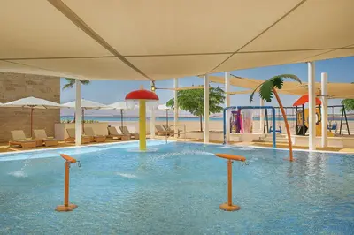 a swimming pool in a resort with chairs and a slide at Hilton Dead Sea Resort & Spa in Sowayma