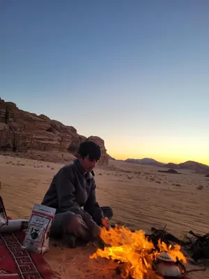 a man sitting next to a fire in the desert at Wadi rum Breeze of calm in Wadi Rum