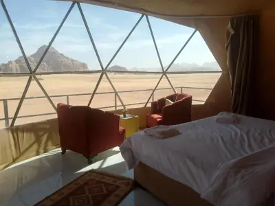 a bedroom with a bed and two chairs and a view of the desert at Wadi Rum Adventure Camp & Tour in Wadi Rum