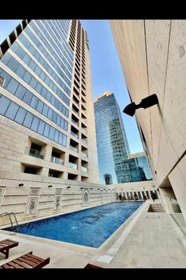 a building with a swimming pool in front of two tall buildings at Pasha Holiday - DAMAC Tower in Amman