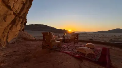 a table and chairs in the desert with the sunset at Wadi rum camp Ausama in Wadi Rum