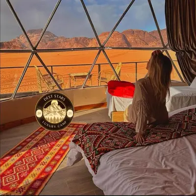 a woman sitting on a bed looking out at the desert at DESRT STARS lUXURY CAMP in Disah