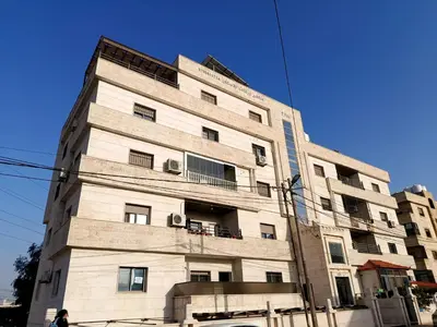 a tall white building with windows on a street at غرفه مفروشه ومكيفه بجانب الكارفور اربد in Irbid