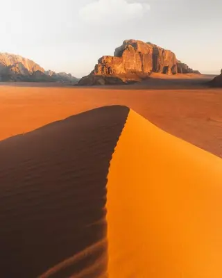 a sand dune in the desert with mountains in the background at A luxurious experience under the stars of Wadi Rum in Wadi Rum