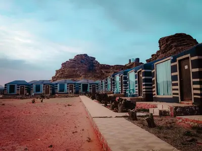 a row of houses on a beach with mountains in the background at Solar Soul Camp - Wadi Rum Desert Experience & Stargazing in Wadi Rum