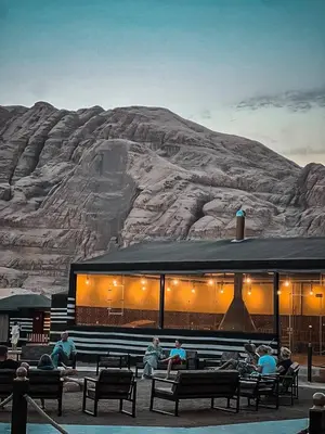 a building with people sitting on benches in front of a mountain at Victoria rum Luxury camp in Disah