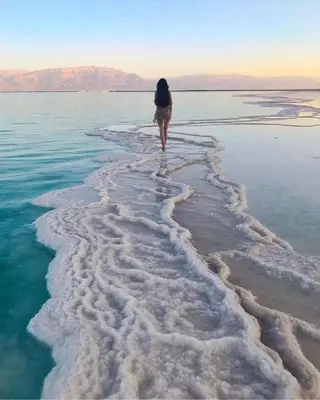 a woman walking through the water on the beach at The Amazing View chalet in Al Rama