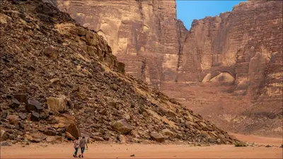 two people walking on the sand near a mountain at Skylight Wadi Rum Camp in Disah