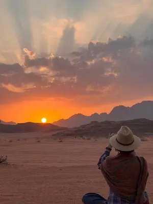 a person sitting in the desert looking at the sunset at Skylight Wadi Rum Camp in Disah
