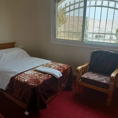 a bedroom with a bed and a chair and a window at Petra Eyes in Wadi Musa