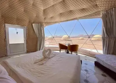 a bedroom with a bed and chairs and a large window at Wadi Rum Nada Camp in Wadi Rum