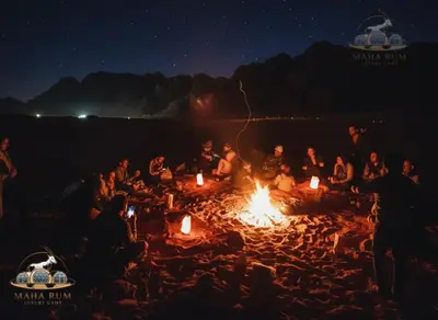 a group of people sitting around a fire on a beach at MAHA Rum Luxury Camp in Disah