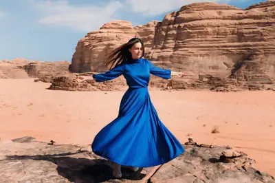 a woman in a blue dress standing on a rock in the desert at Wadi Rum Guide , Luxury Camp
