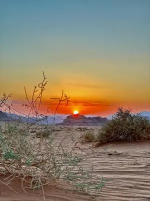 a sunset in the desert with the sun setting at Wadi Rum Mountains in Wadi Rum
