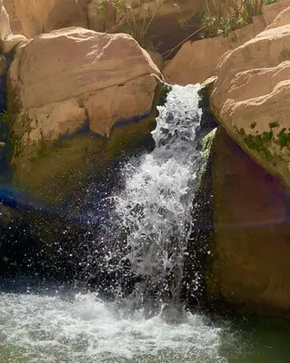a waterfall in a pool of water next to rocks at Dana Trail Nomad Camp in Dana