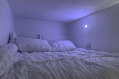 an unmade bed in a bedroom with a purple light at Modern Loft Studio Panoramic Views And Smart Design in Amman