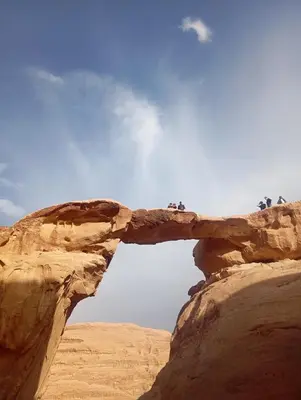 an arch in the desert with people standing on it at Wadi rum bubble camp in Wadi Musa