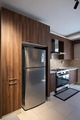 a kitchen with a stainless steel refrigerator and wooden cabinets at Der Ghbar 3BR - 2 Terraces, Scenic Views & BBQ in Amman