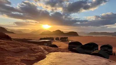 a sunset in the desert with a group of camels at Wadi Rum Desert Night Camp in Wadi Rum