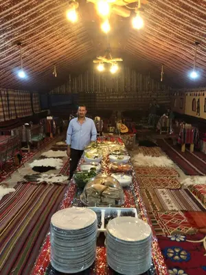 a man standing in front of a table with plates at Khaled's Camp - Wadi Rum in Wadi Rum