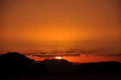 a sunset in the desert with the sun hiding behind a cloud at Khaled's Camp - Wadi Rum in Wadi Rum