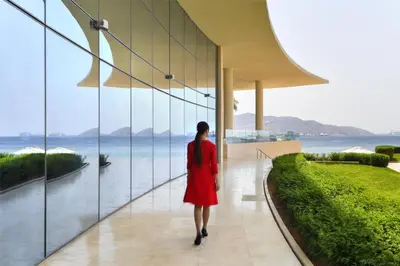 a woman in a red dress walking down a hallway looking at the water at Kempinski Hotel Aqaba in Aqaba