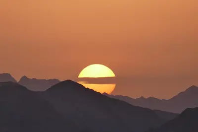 a sunset over mountains with the sun in the sky at Jordan Tracks Bedouin Camp in Wadi Rum