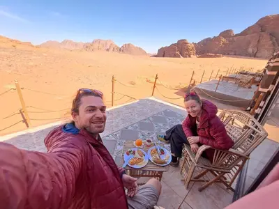a man and a girl sitting at a table in the desert at Wadi Rum Sky Tours & Camp in Wadi Rum