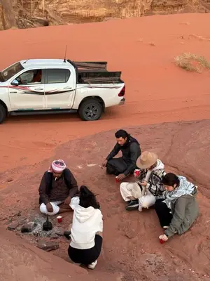 a group of people sitting in the desert with a car at Wadi Rum Sky Tours & Camp in Wadi Rum