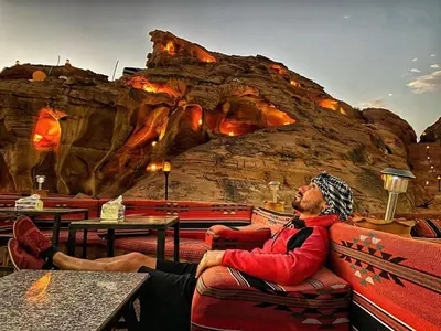 a man sitting in a chair in front of a mountain at Wadi Rum Dream Camp in Wadi Rum
