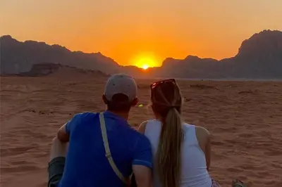 a man and a woman sitting in the desert watching the sunset at Welcome to Wadi Rum Camp in Wadi Rum