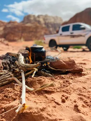 a fire in the dirt with a truck in the background at Welcome to Wadi Rum Camp in Wadi Rum