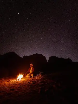 a person sitting next to a fire at night at Stargazing Camp & Tours in Wadi Rum