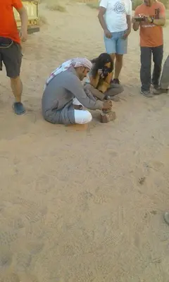 a person kneeling on the sand with a dog at Rumshines Camp in Wadi Rum