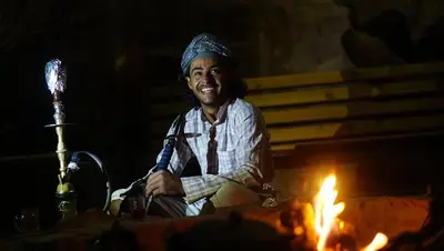 a man is sitting next to a fire at Rumshines Camp in Wadi Rum