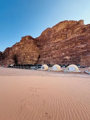 a desert with a rock wall and footprints in the sand at DESERT HELO lUXURY CAMP & TOUR in Wadi Rum