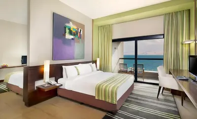a hotel room with a bed and a desk and a television at Holiday Inn Resort Dead Sea by IHG in Sowayma