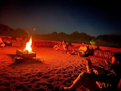 a group of people sitting around a fire on a beach at Wadi Rum Desert Camp in Wadi Rum