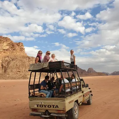 a group of people riding in the back of a truck in the desert at Wadi Rum Desert Camp in Wadi Rum