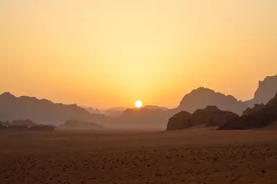 a sunset in the desert with the sun setting at Wadi Rum Fire Camp in Wadi Rum