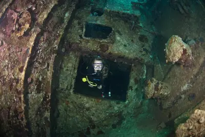 a diver is looking through a hole in a shipwreck at Aqaba Adventure Divers Resort & Dive Center in Aqaba