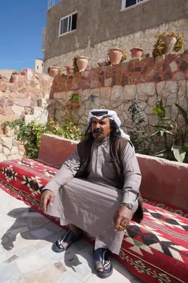 an older man sitting on a bench on a rug at Happy Bedouin House Petra in Al Ḩayy