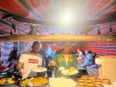 two men standing at a table with plates of food at Happy Bedouin House Petra in Al Ḩayy