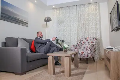 a man sitting on a couch in a living room at Almond Hotel Apartments in Amman