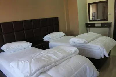 a room with three beds with white sheets and a mirror at Al haramain Furnished Apartments in Amman