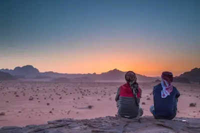 two people sitting in the desert watching the sunset at Desert Rock camp in Wadi Rum