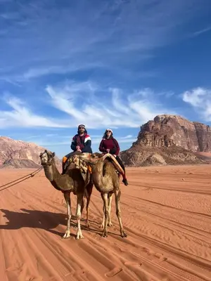 two people riding on the backs of camels in the desert at Desert Rock camp in Wadi Rum