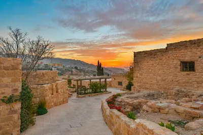 a sunset over a city with stone buildings and flowers at The Old Village Hotel & Resort in Wadi Musa
