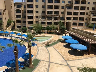 a pool with blue umbrellas and palm trees and a building at Apartment Samarah Resort Sea & Pool view D in Sowayma