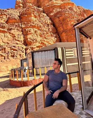 a man sitting on a railing in front of a mountain at Joy to Wadi Rum in Wadi Rum